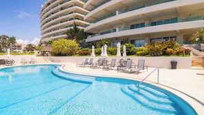 A swimming pool with lounge chairs and umbrellas, surrounded by a building with balconies and a landscaped garden. - Ocean Terrace 3 Habitaciones (Nuevo nayarit)