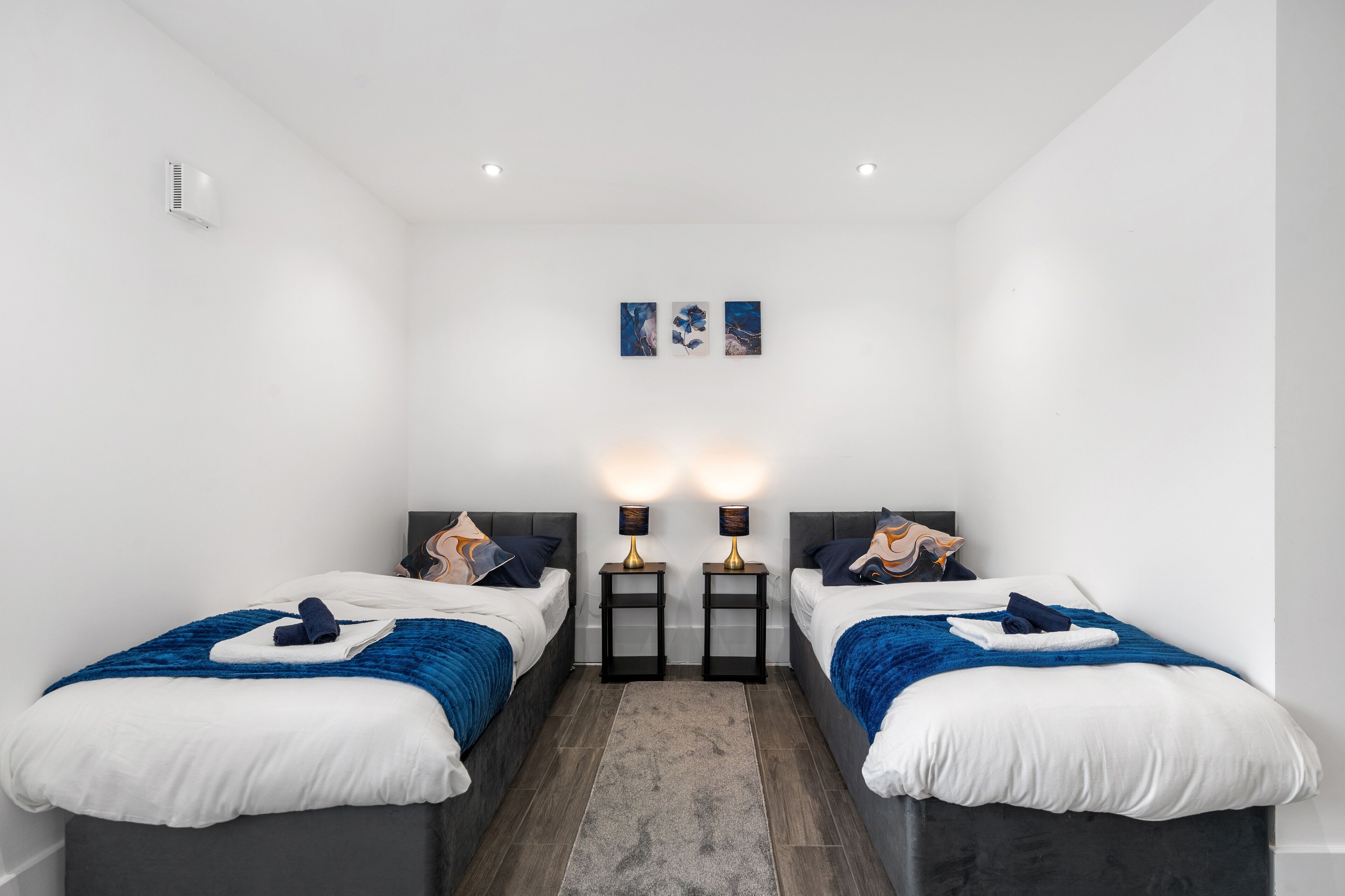 Habitación de hotel con dos camas, una alfombra gris y lámparas fijadas a la pared.