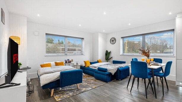 A modern living room with a sofa set, a dining table with chairs, a TV, and large windows with blinds. - Modern | City Stay | Walk to Station| Free Parking (Brighton and Hove)