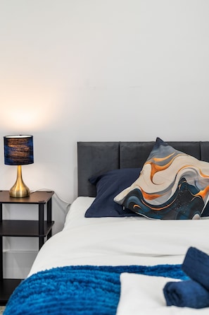 A neatly made bed with a blue blanket, a decorative pillow, and a bedside lamp on a nightstand. - Modern | City Stay | Walk to Station| Free Parking (Brighton and Hove)