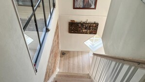 Eine Treppe mit Holzdielen und Metallgeländer, die zu einer Zwischenebene führt, auf der verschiedene Gegenstände an einer Wand ausgestellt sind.
