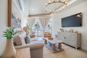 A spacious living room with a sofa, a coffee table, and a TV mounted on the wall. - Styles Beach 2A - Luxury Beachfront Condo w/ Pool (San Pedro)