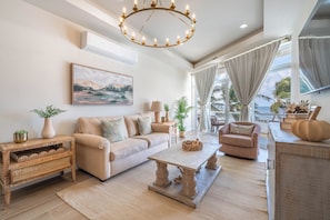 A spacious living room with a sofa, a coffee table, and a view of the ocean through large windows. - Styles Beach 2A - Luxury Beachfront Condo w/ Pool (San Pedro)