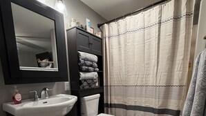 A modern bathroom with a black vanity, white sink, and toilet. There are towels stacked on the vanity and a shower curtain with a striped pattern. - Cozy 1-bedroom apartment in delightful Arlington  (Arlington)