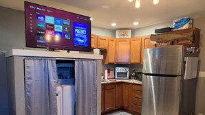 A modern kitchen with a built-in TV displaying streaming services, wooden cabinets, a stainless steel refrigerator, and a compact washer-dryer unit. - Cozy 1-bedroom apartment in delightful Arlington  (Arlington)