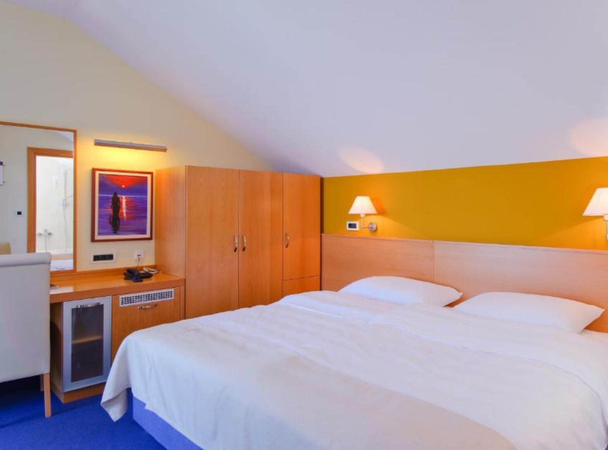 Une chambre d’hôtel équipée d’un lit, d’un bureau, d’un miroir et d’une lampe fixée au mur.