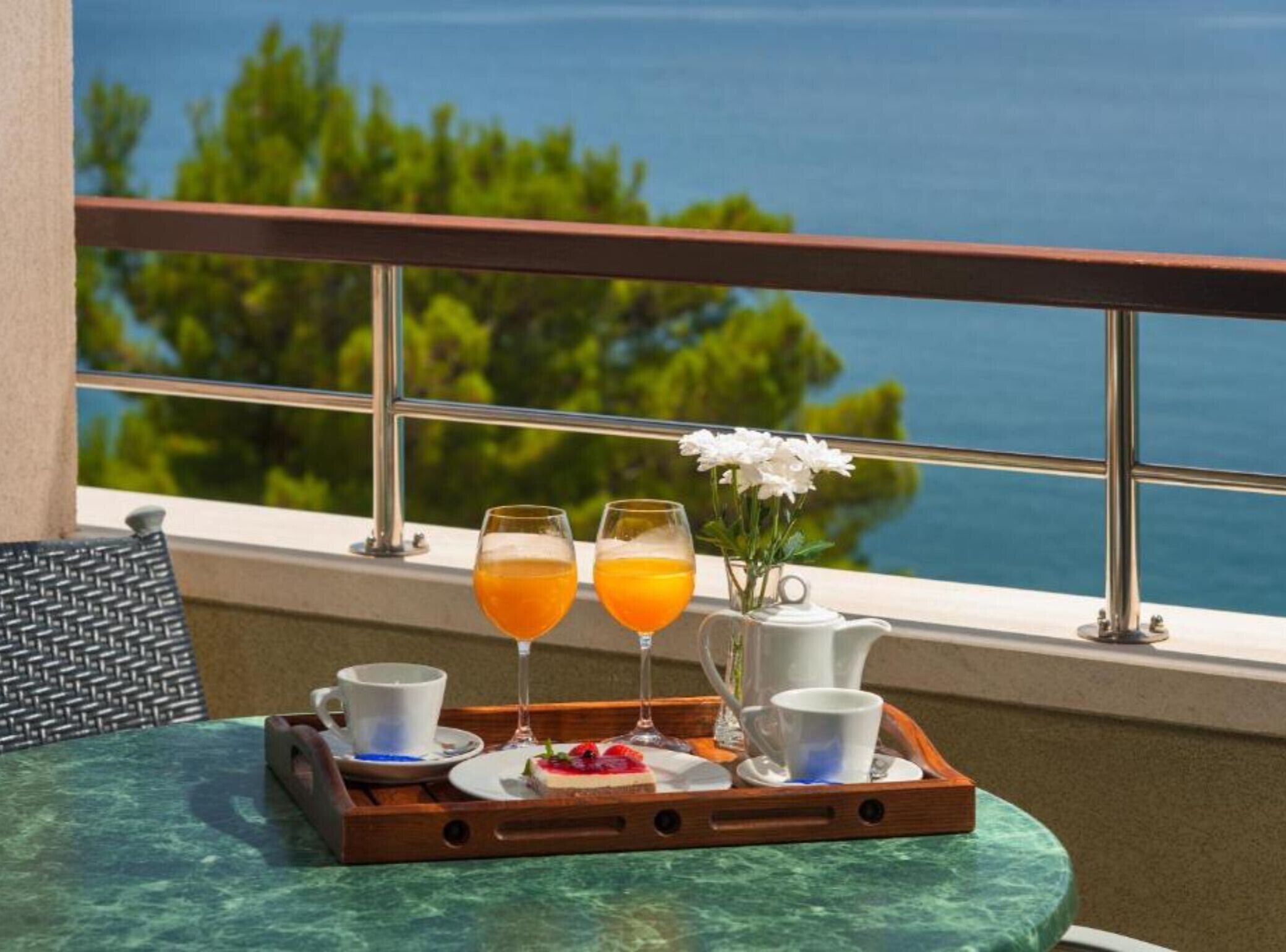 A balcony with a table set for breakfast, including two glasses of orange juice, a cup of coffee, and a teapot.