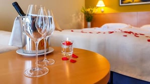 A hotel room with a bed, a bedside table with two wine glasses and a candle, and a painting on the wall. - Panorama Suite With Private Bathroom (Gradac)