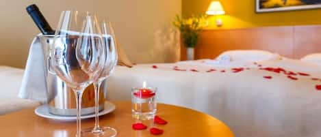 A hotel room with a bed, a bedside table with two wine glasses and a candle, and a painting on the wall.