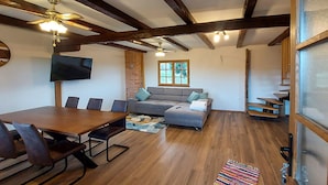 Un espacio habitable amplio con una mesa de comedor de madera, sofá gris y televisor montado en la pared.