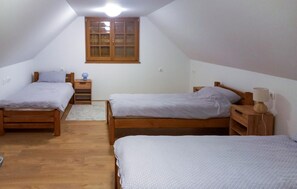 A small, well-lit attic bedroom with two wooden beds, a nightstand with a lamp, and a window with wooden shutters. - Awesome home in Karlovac with WiFi (Karlovac)