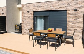 Une terrasse extérieure avec une table et des chaises en bois, un barbecue et un panier de fruits.