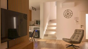 Een moderne woonkamer met een flatscreen-tv, een comfortabele fauteuil, een trap en een wandklok.