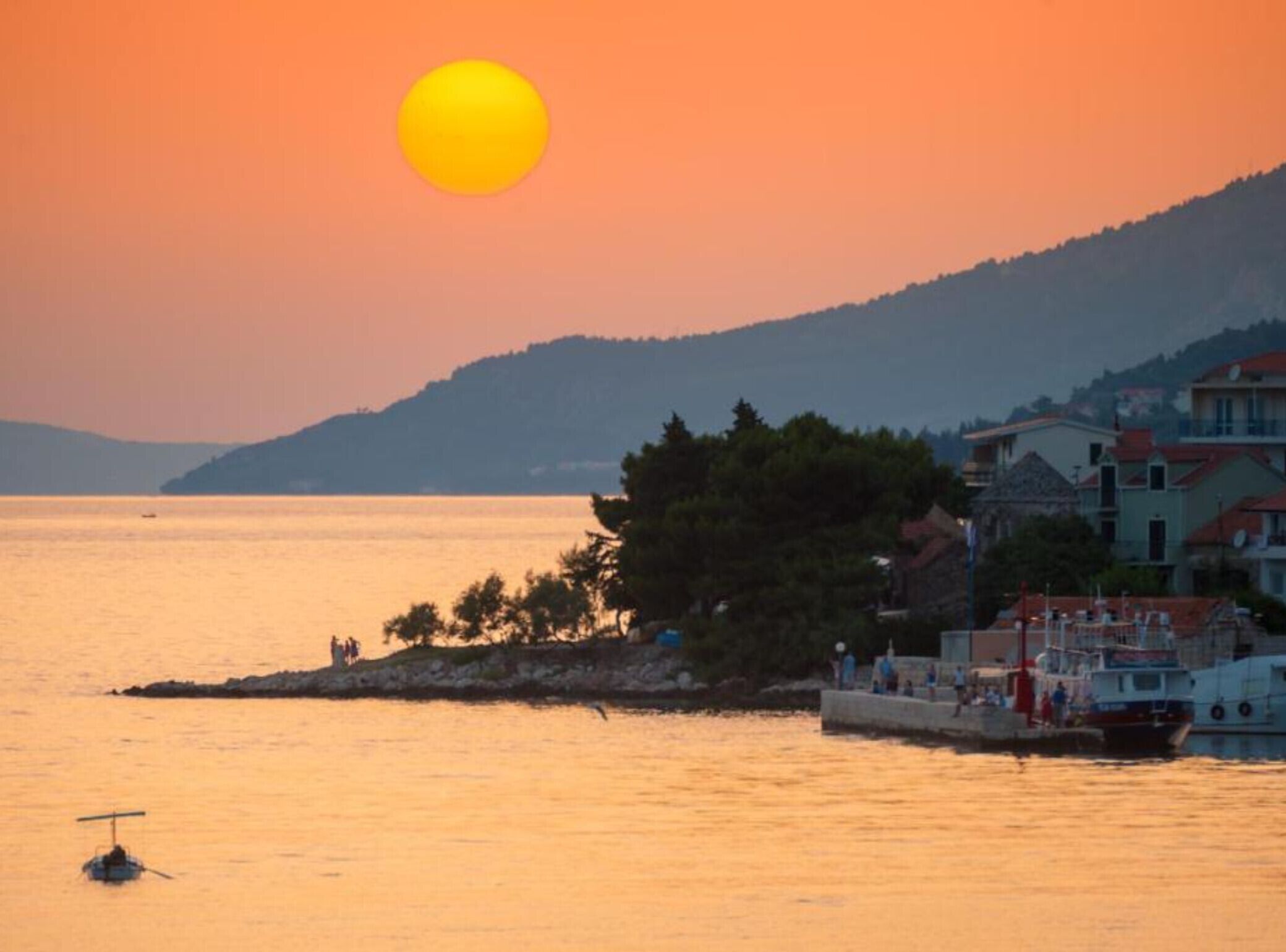 Un coucher de soleil sur la côte, avec un bateau amarré près de bâtiments.