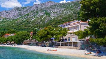 A coastal hotel with a beach, clear waters, and a mountainous backdrop.