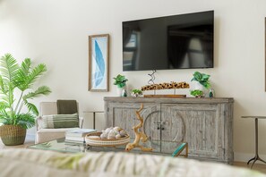 A living room with a sofa, a coffee table, a television mounted on the wall, and a cabinet with decorative items. - Styles Beach 2D - Multi Level Ocean View Condo (San Pedro)
