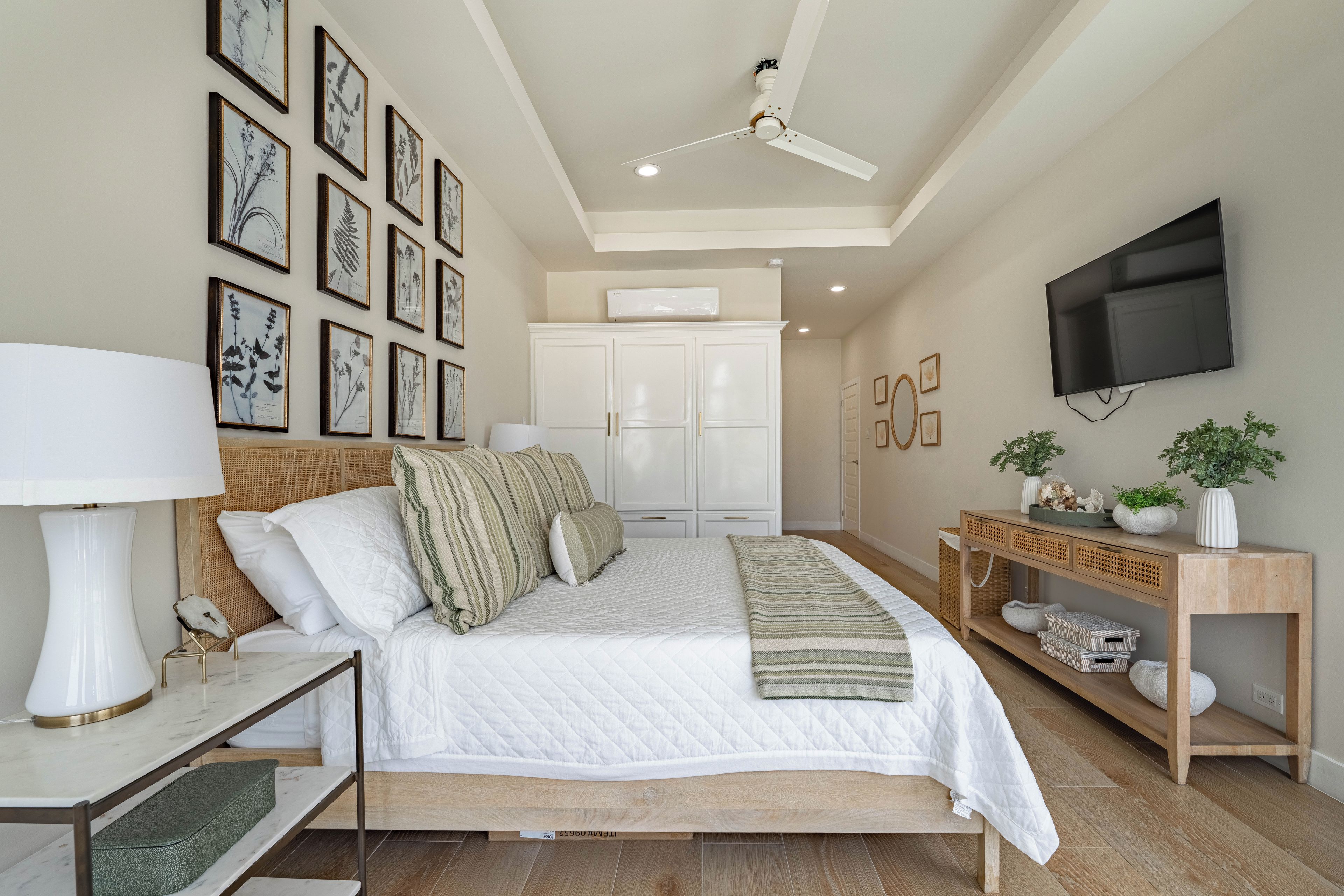Un dormitorio con una cama, mesitas de noche, un ventilador de techo, un televisor e impresiones enmarcadas con motivos botánicos en la pared.