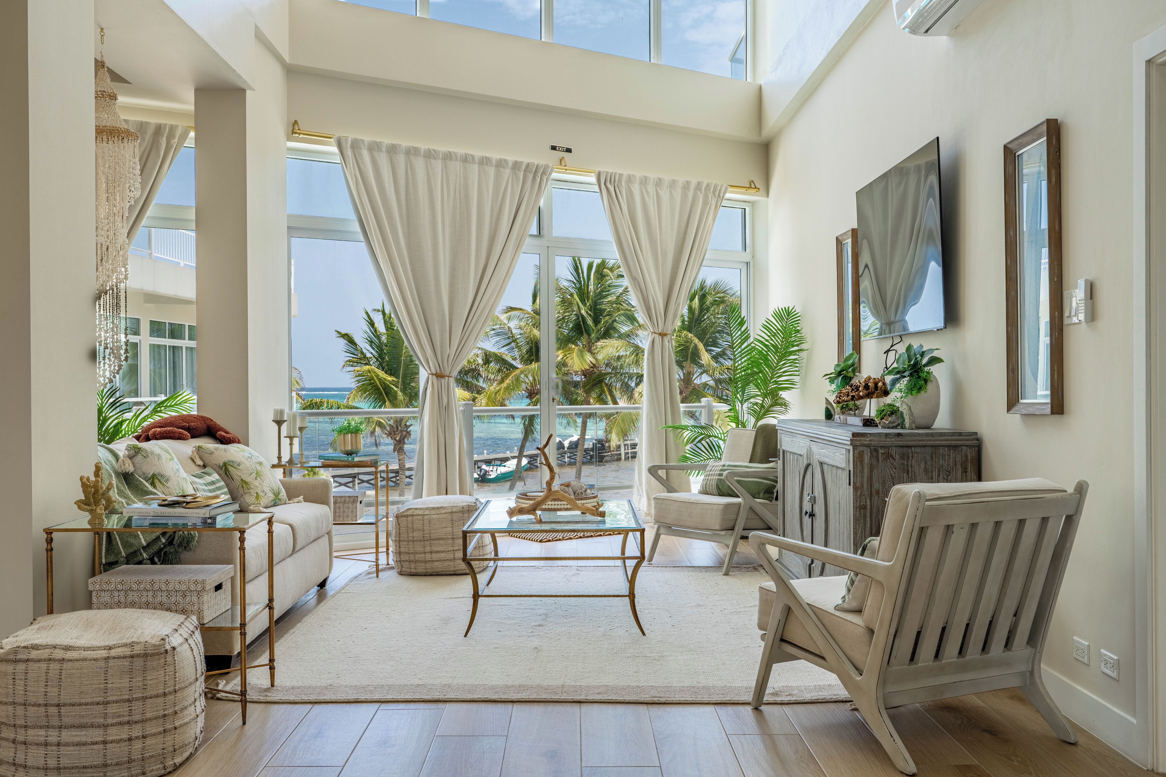 A spacious living room with a large window overlooking a beach, furnished with a sofa, chairs, and a coffee table.