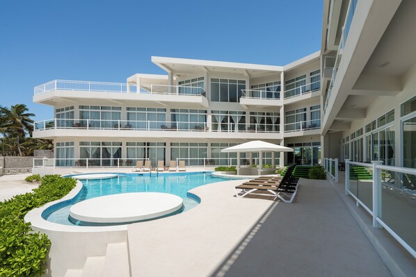 Ein modernes Hotel mit Schwimmbad, mehreren Balkonen und blauem Himmel.