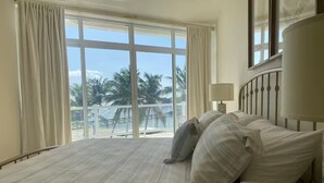 Een hotelkamer met een groot bed, een nachtkastje en uitzicht op palmbomen en een balkon.