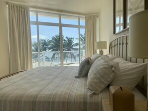 Ein Hotelzimmer mit einem großen Bett, einem Nachttisch und Blick auf Palmen und einen Balkon.