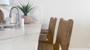 Een moderne keuken met een groot keukenblok, een roestvrijstalen spoelbak en houten stoelen met geweven rugleuningen.