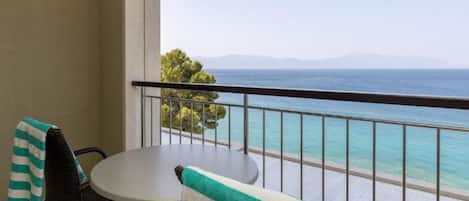Un balcó amb taula i cadires, amb vista al mar turquesa i muntanyes llunyanes.