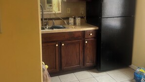 A kitchen with wooden cabinets, a black refrigerator, a window with blinds, and a tiled floor. - Welcoming 1-bedroom apartment with AC in charming Jackson (Jackson)