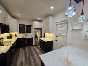 A modern kitchen with white cabinets, a stainless steel refrigerator, and a marble countertop.