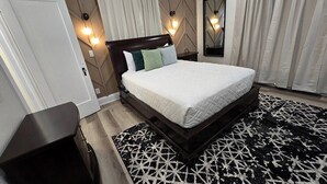 Ein Schlafzimmer mit einem großen Bett, einem dunklen Kopfteil, einem Teppich mit geometrischem Muster und zwei Wandleuchten.