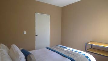 A bedroom with a bed, a door, and a shelf with lights.