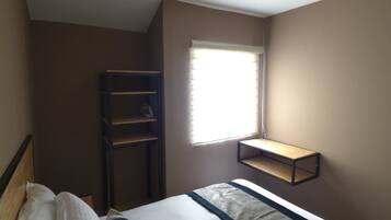A bedroom with a bed, a window, a shelf, and a wardrobe.