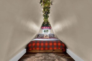 A bedroom with a sloped ceiling, a bed with a checkered bedspread, a small bedside table, and a window.