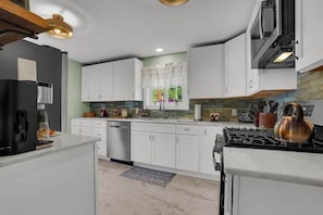 A modern kitchen with white cabinets, a stove, a kettle, and a window with curtains.