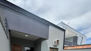 Una casa moderna con facciata grigia, porta in legno, piccolo giardino e vialetto in cemento.