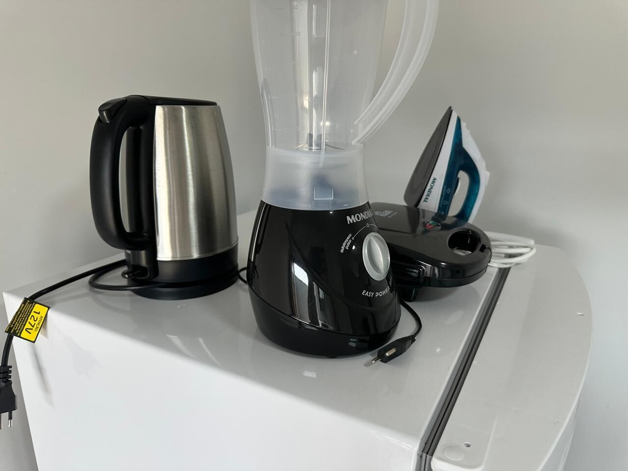 A kitchen with a blender, kettle, and iron on a white countertop.