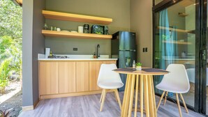 A modern kitchen with wooden cabinets, a built-in refrigerator, and a dining area with a round table and two chairs. - Mira Bungalow (Punta Uva)