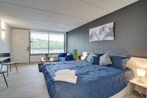 Ein modernes Schlafzimmer mit einem großen Bett, einem Schreibtisch und Blick auf Grün durch ein Fenster.