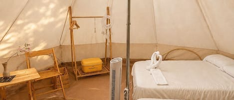 Tienda con dos camas, una mesa, una silla, una lámpara colgante y un ventilador.
