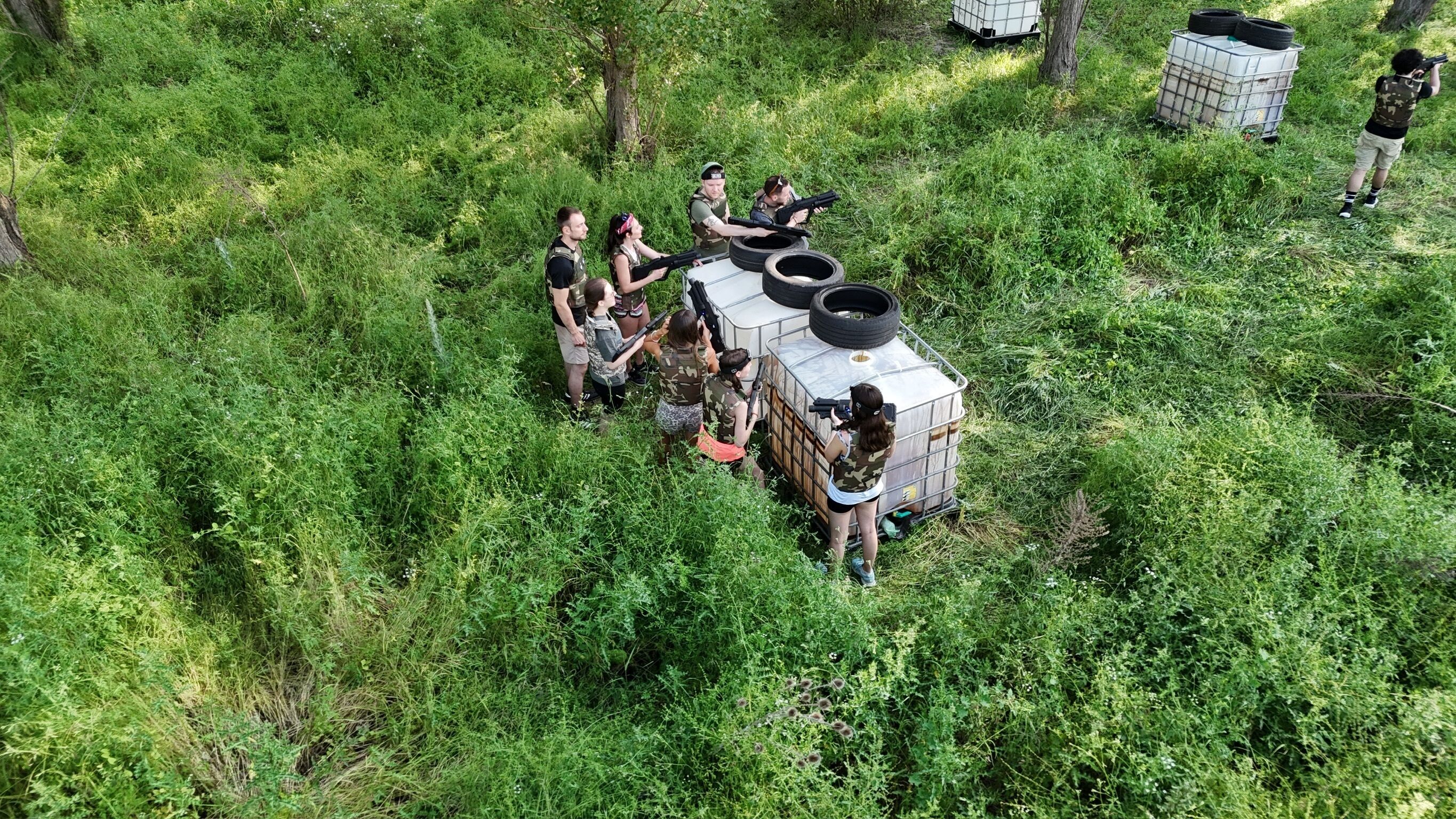 A group of people in a forested area with a large, white, rectangular structure with tires on top, surrounded by dense green foliage.