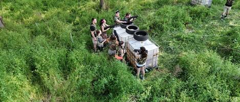 A group of people in a forested area with a large, white, rectangular structure with tires on top, surrounded by dense green foliage.
