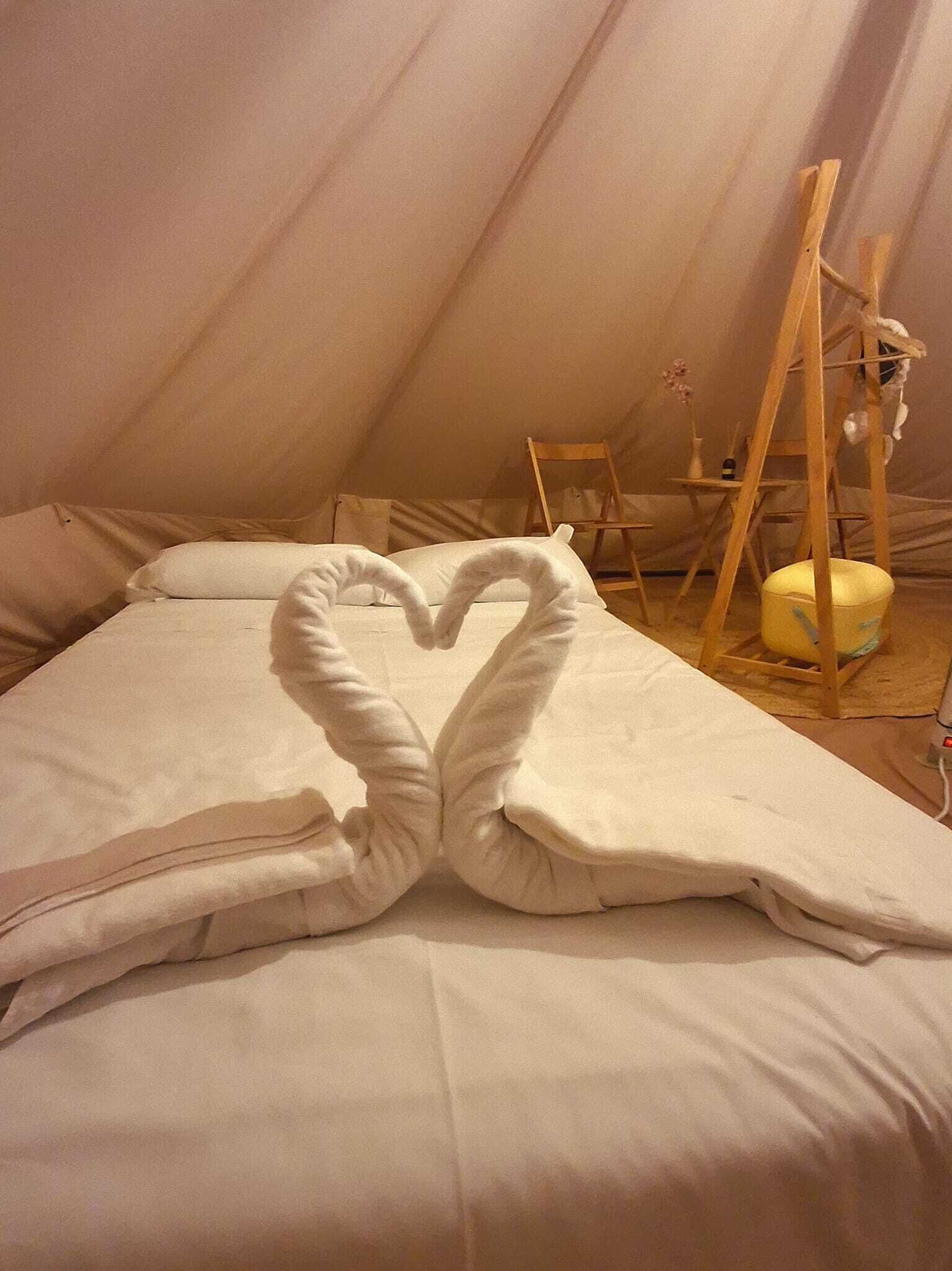 A cozy room with a bed, a heart-shaped towel on the bed, a wooden ladder, and a small table with a vase.