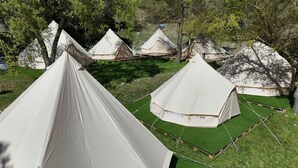 Varias tiendas en forma de cúpula dispuestas en un camping con césped artificial verde y árboles al fondo.