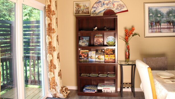 A dining area with a table set for two, a bookshelf with cookbooks, and a view through a glass door. - Superb 5-bedroom house with large 8000 SF lot in Seattle suburb for your getaway (Mountlake Terrace)