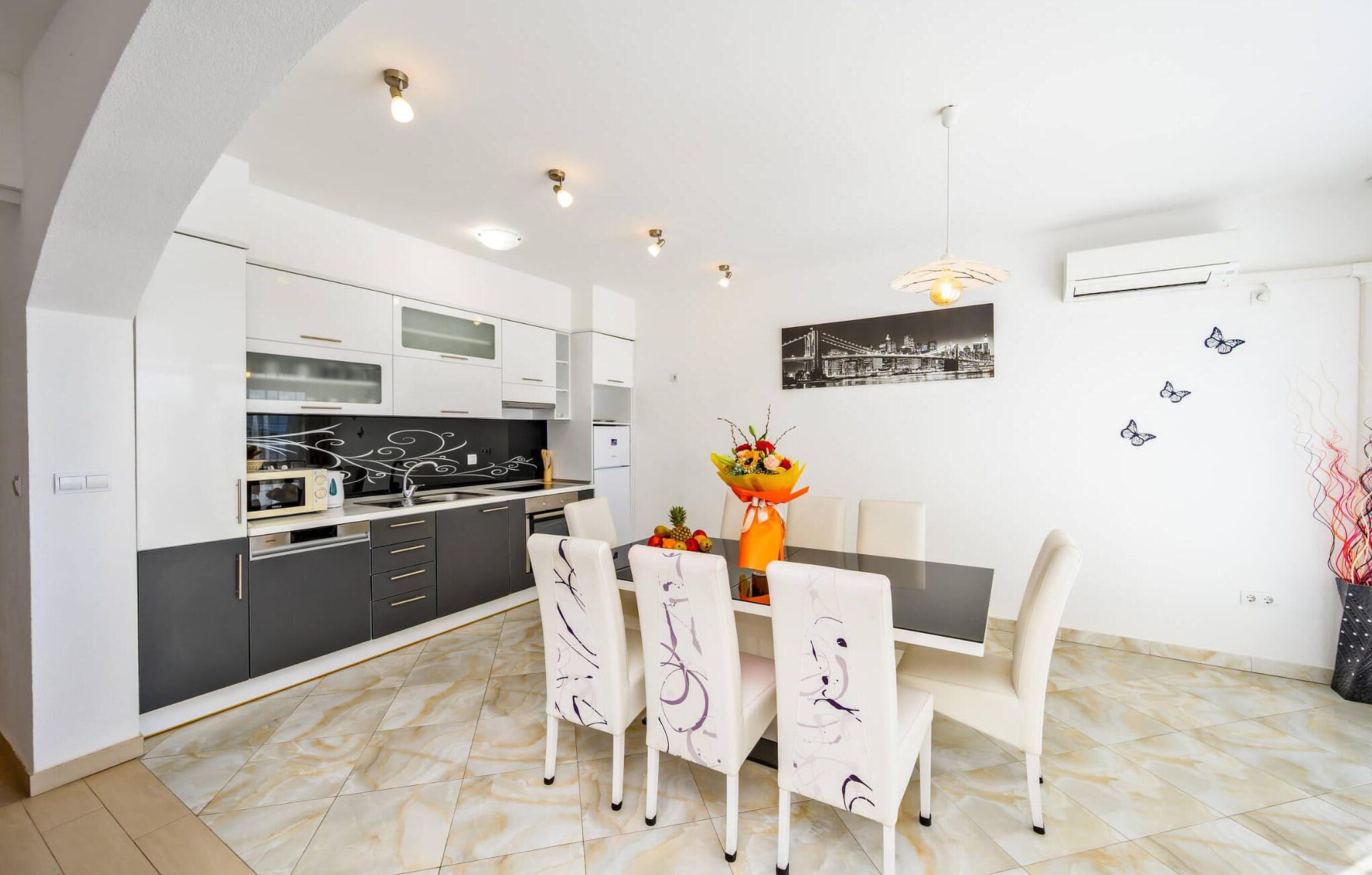 Una cocina moderna con armarios blancos, una mesa de comedor con sillas y una obra de arte urbana en la pared.