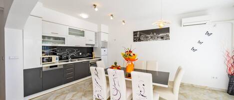 Una cocina moderna con armarios blancos, una mesa de comedor con sillas y una obra de arte urbana en la pared.