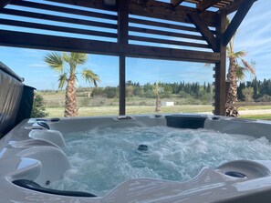 Un jacuzzi con una pérgola de madera encima, rodeado de palmeras y vistas a un paisaje rural.