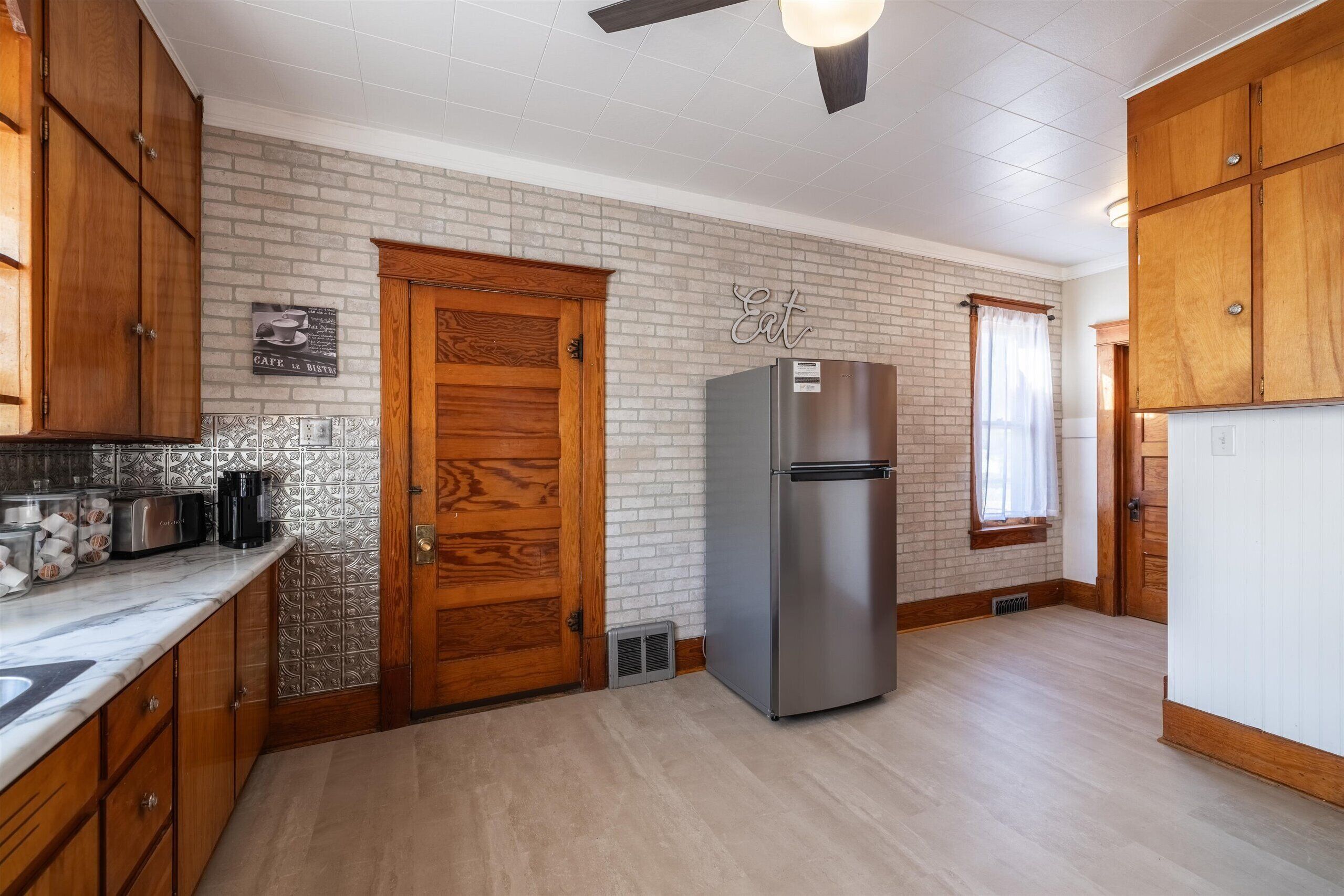 Una cocina con armarios de madera, un refrigerador de acero inoxidable, salpicadero de azulejos y una puerta de madera.