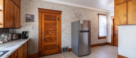 Una cocina con armarios de madera, un refrigerador de acero inoxidable, salpicadero de azulejos y una puerta de madera.