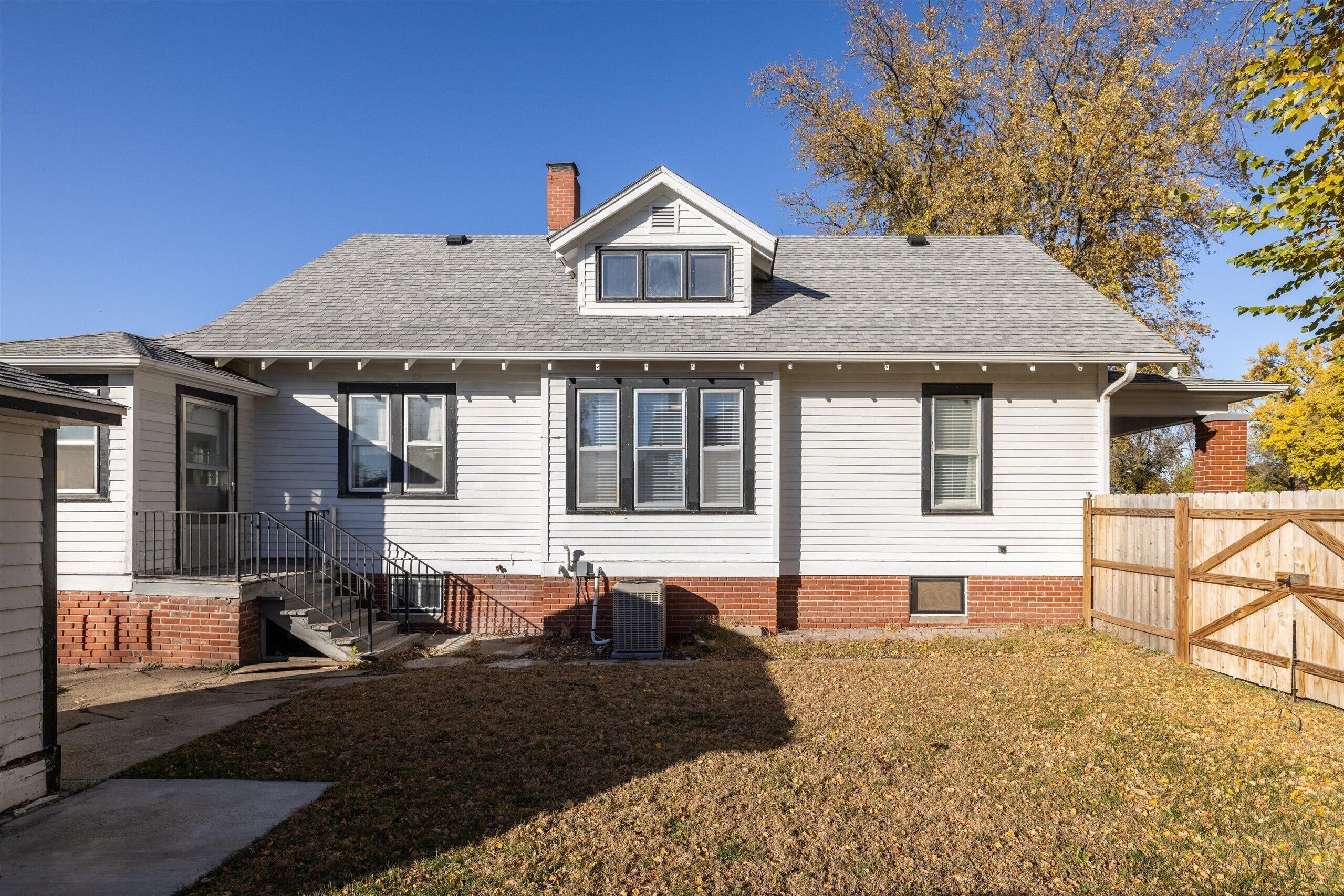A two-story house with a front porch, a brick foundation, and a fenced yard.
